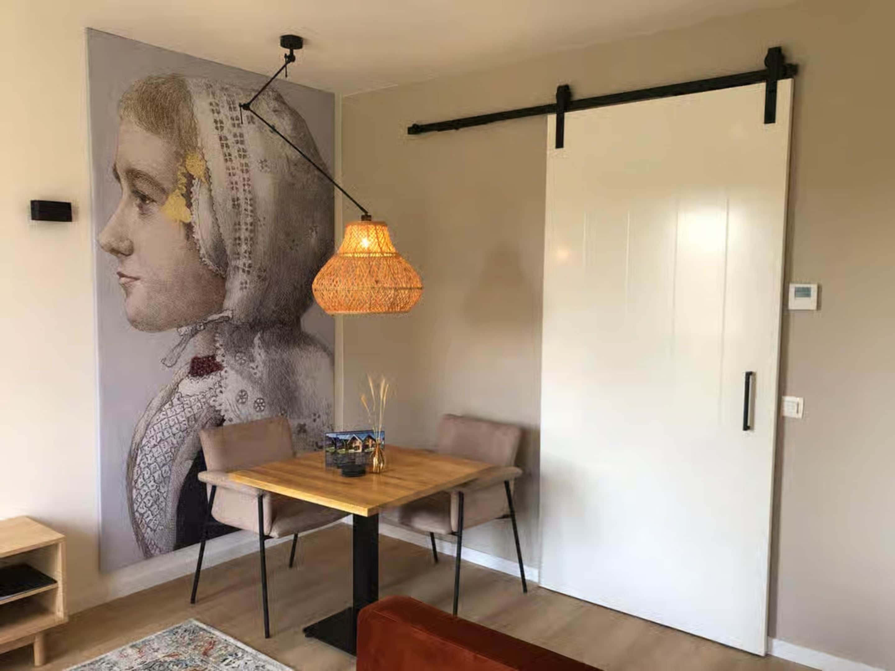 Een eetruimte met een tafel, stoelen, een wandlamp en een schuifdeur.