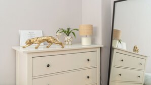 En vit byrå med tre lådor, en guldfärgad leopardfigur, en växt och en lampa.