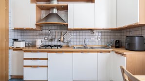 Ett modernt kök med vita skåp, en bänkskiva i trä, en gasspis, ett handfat och en kaffebryggare.