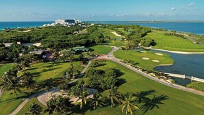 Une vue aérienne d’un terrain de golf avec un plan d’eau, des palmiers et un grand bâtiment en arrière-plan.