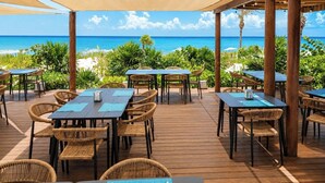 Un espace extérieur aménagé pour les repas, avec des tables et des chaises, offrant une vue sur une plage et l’océan.
