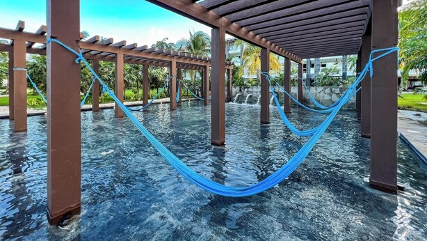 Un hamac suspendu sous une pergola en bois, au-dessus d’une piscine.