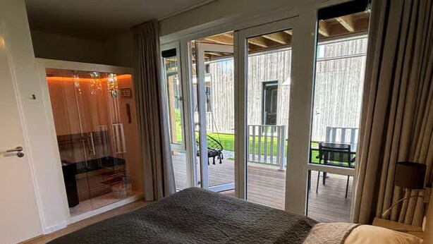 A bedroom with a large bed, a sliding glass door leading to an outdoor deck with a table and chairs. - Lavish Lodge With Private Sauna (Zoutelande)