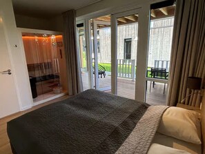 Et soveværelse med en stor seng, en skydedør til en udendørs terrasse med et bord og stole.