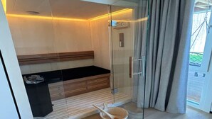 A modern spa room with a glass-enclosed shower, wooden bench, and a small wooden basin. - Lavish Lodge With Private Sauna (Zoutelande)