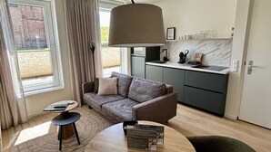 A modern living room with a sofa, a round table, and a kitchen area with a marble countertop. - Lavish Lodge With Private Sauna (Zoutelande)
