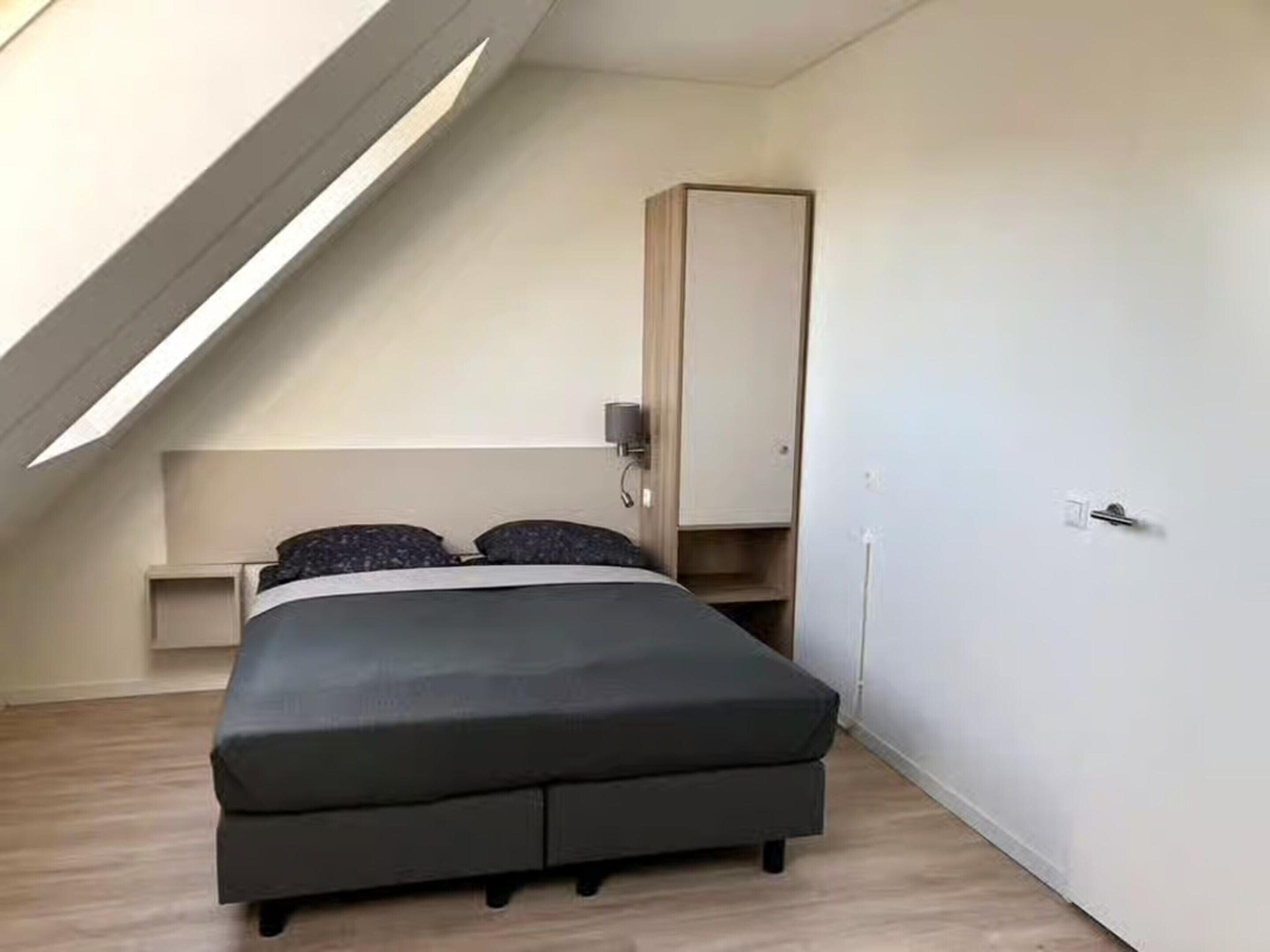 Une chambre à coucher de taille réduite, avec un plafond en pente, un lit, une armoire et une petite table de chevet.