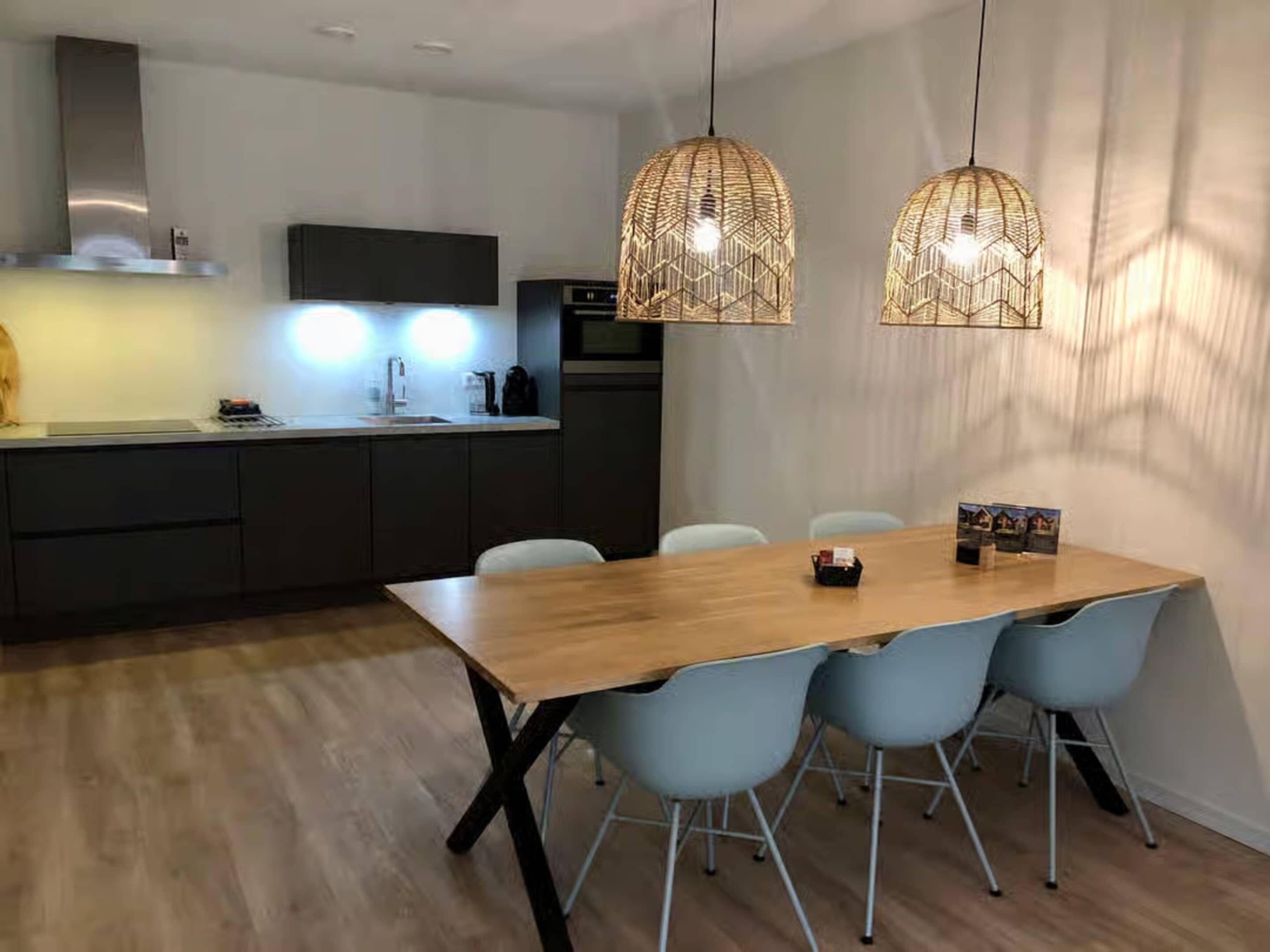 Een moderne keuken met donkere kastjes, een houten eettafel en lichtblauwe stoelen.