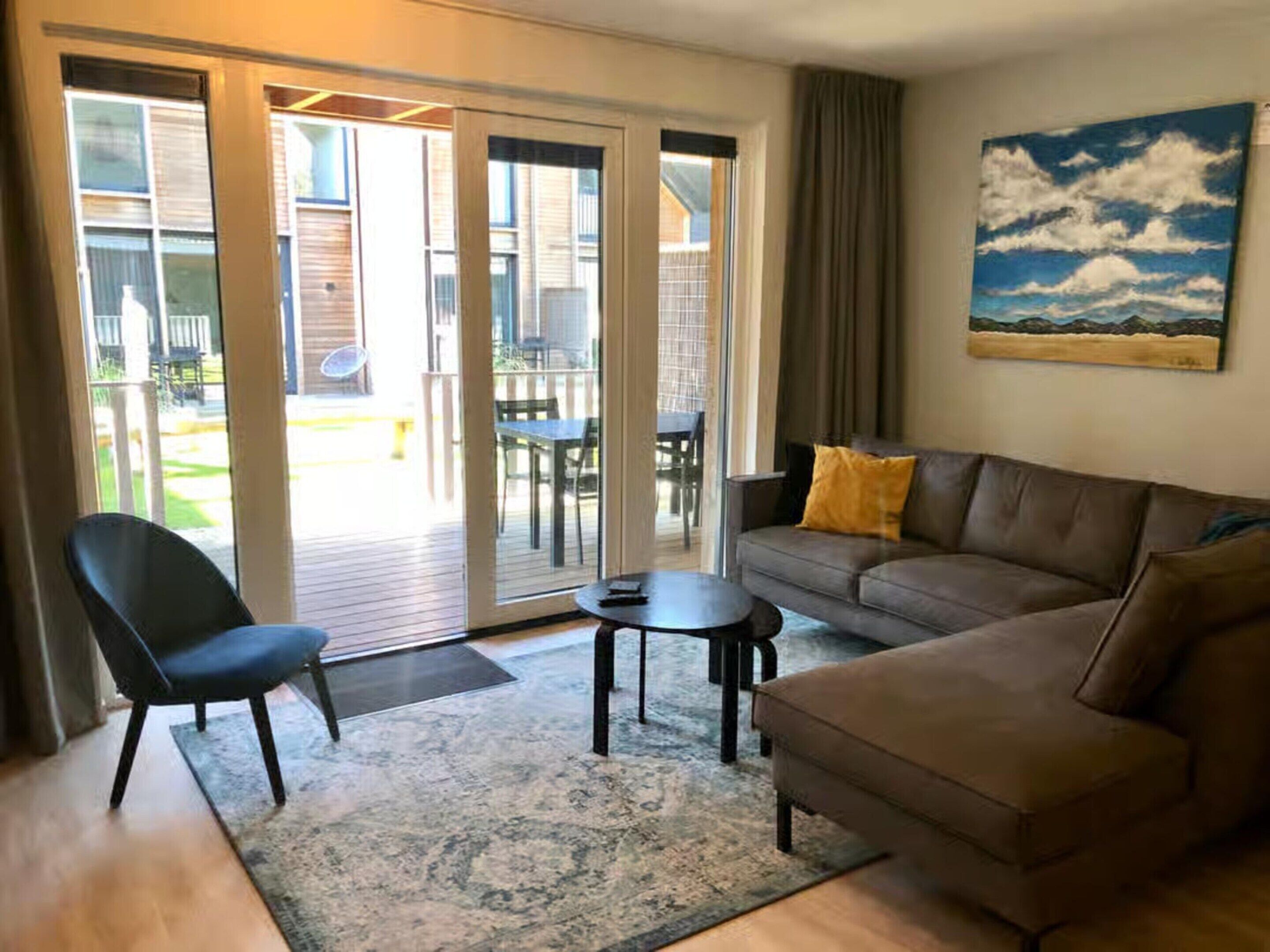 A living room with a brown sofa, a black chair, a small table, and a large window with a view of the outdoors.