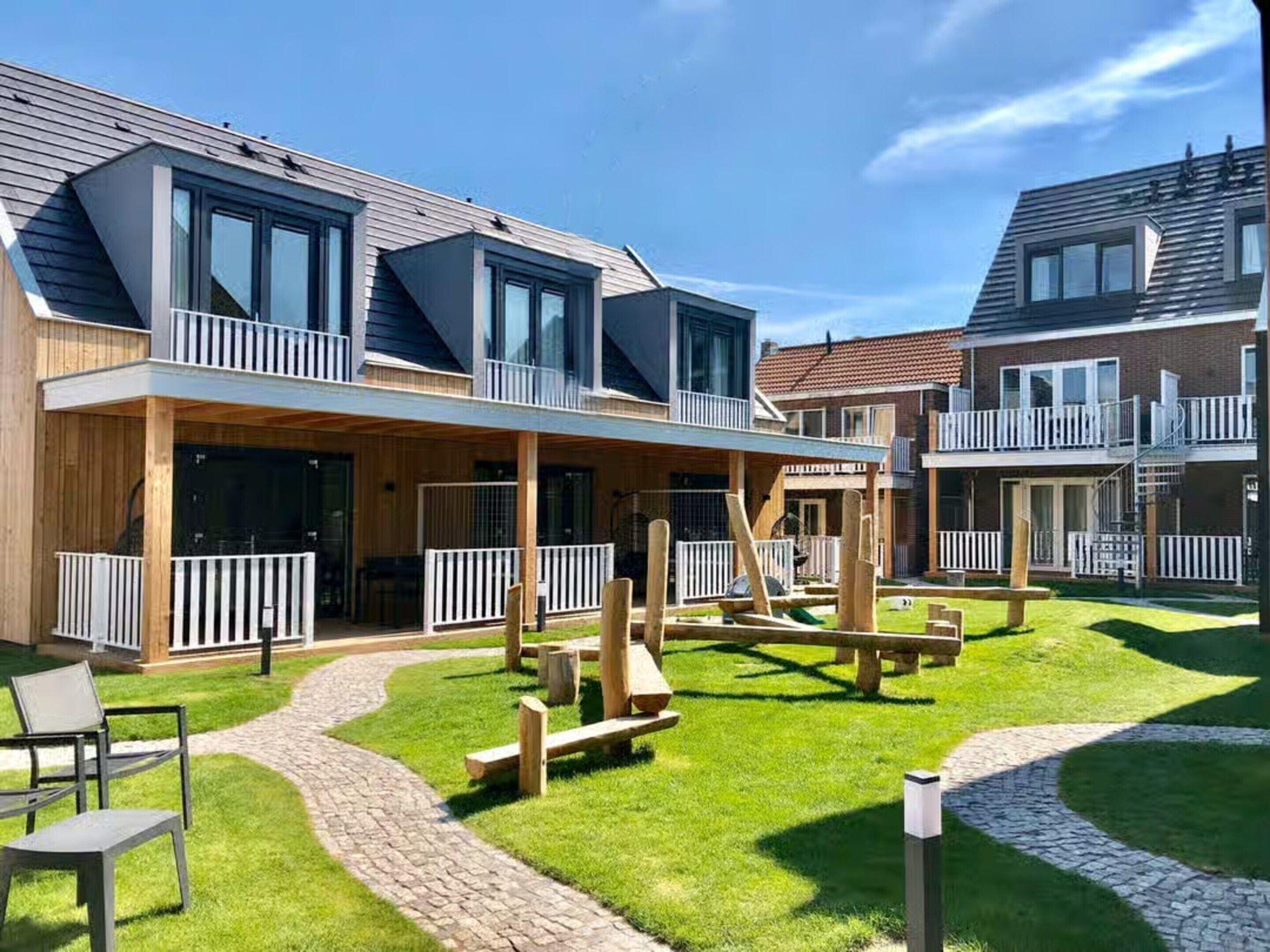 Un edificio residencial moderno con un patio cubierto, mobiliario exterior y un césped bien cuidado.