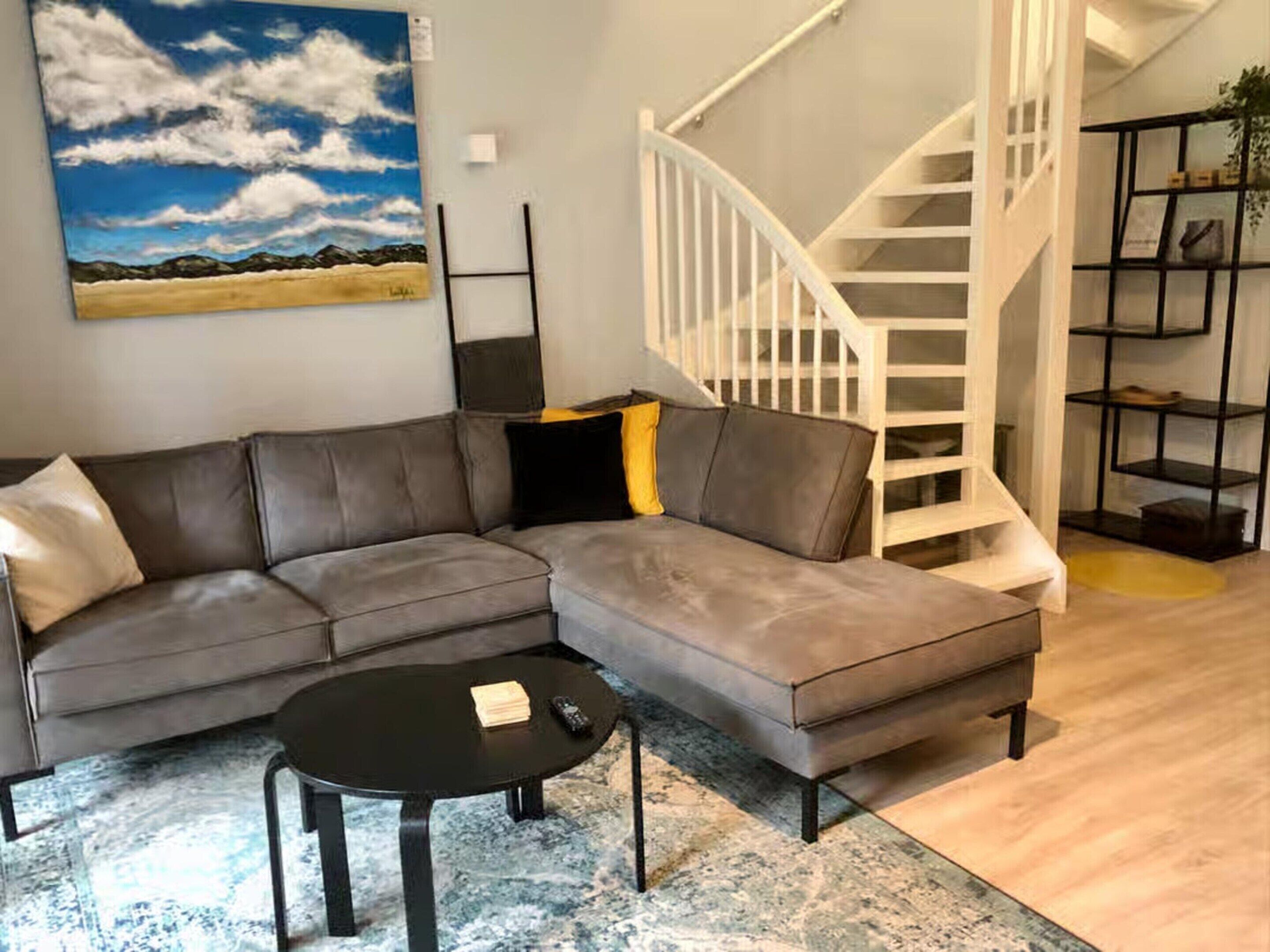 A modern living room with a grey sectional sofa, a black coffee table, and a white spiral staircase.