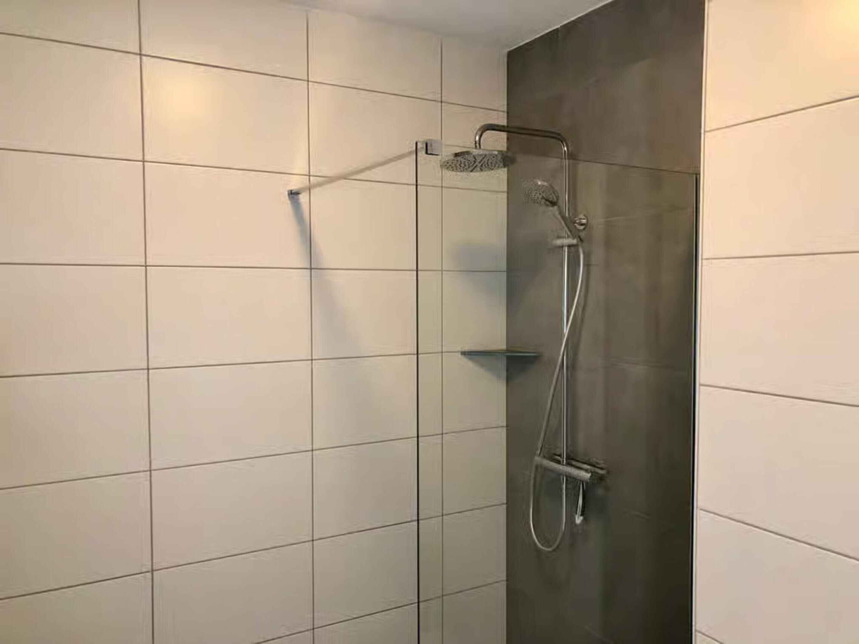 A shower with a handheld showerhead and a wall-mounted faucet.