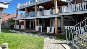 Um edifício residencial de dois andares com varanda em cada pavimento, um alpendre coberto e um caminho de acesso pavimentado.