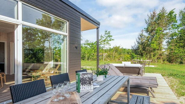 Eine Terrasse im Freien mit Holzmöbeln, einem Buch mit dem Titel '1864' und einem Glastisch.