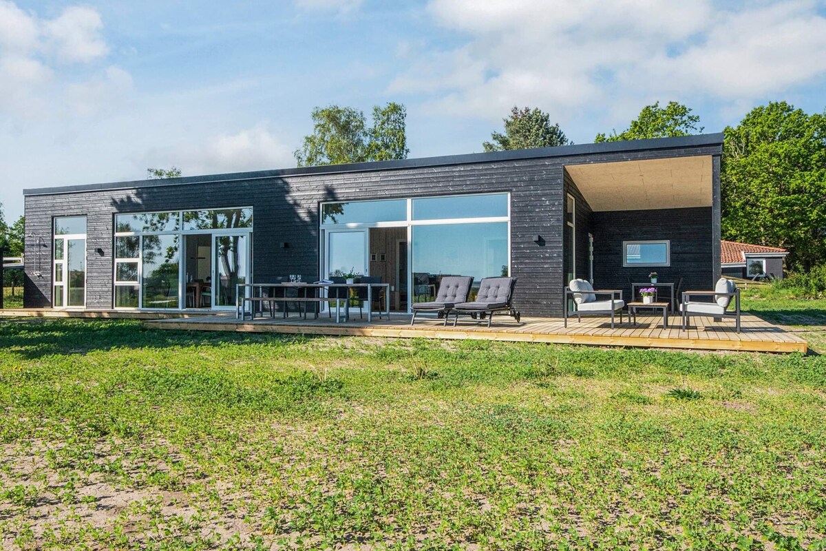 Ein modernes Haus mit großen Glasfenstern, einer Terrasse mit Gartenmöbeln und einem Rasen.