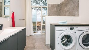Ein moderner Waschraum mit zwei Waschmaschinen mit Frontlader, einem großen Fenster und Blick ins Freie.