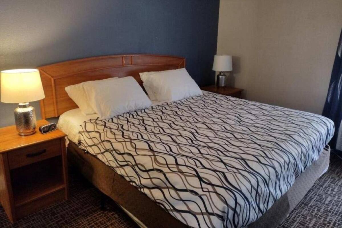 A hotel room with a large bed, a wooden headboard, two bedside tables with lamps, and a patterned bedspread.