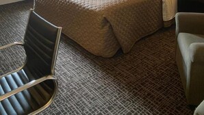 A hotel room with a large bed, two bedside lamps, a window with curtains, a radiator, and two chairs. - Fairview Inn Airport (Greensboro)