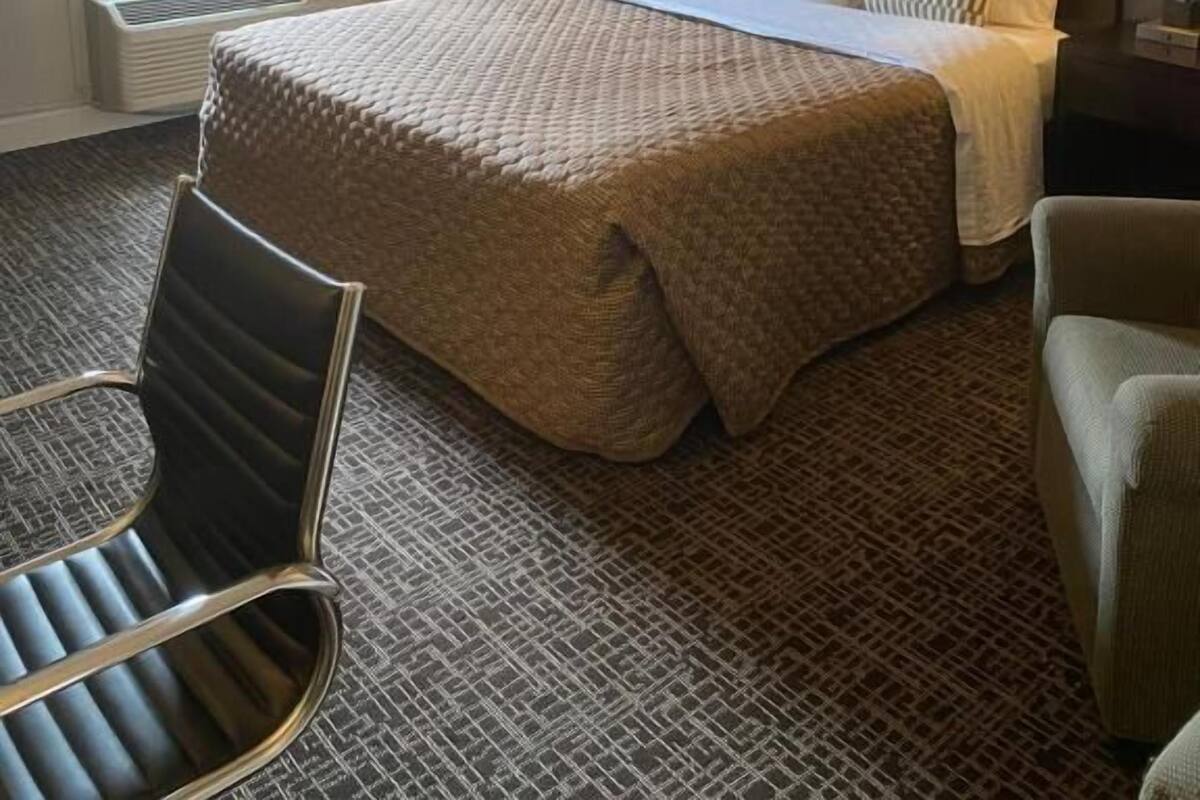 A hotel room with a large bed, two bedside lamps, a window with curtains, a radiator, and two chairs.