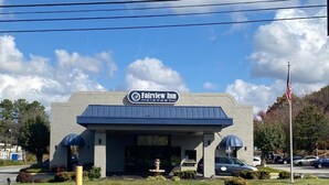A Fairview Inn building with a sign, parking lot, and American flag. - Fairview Inn Airport (Greensboro)