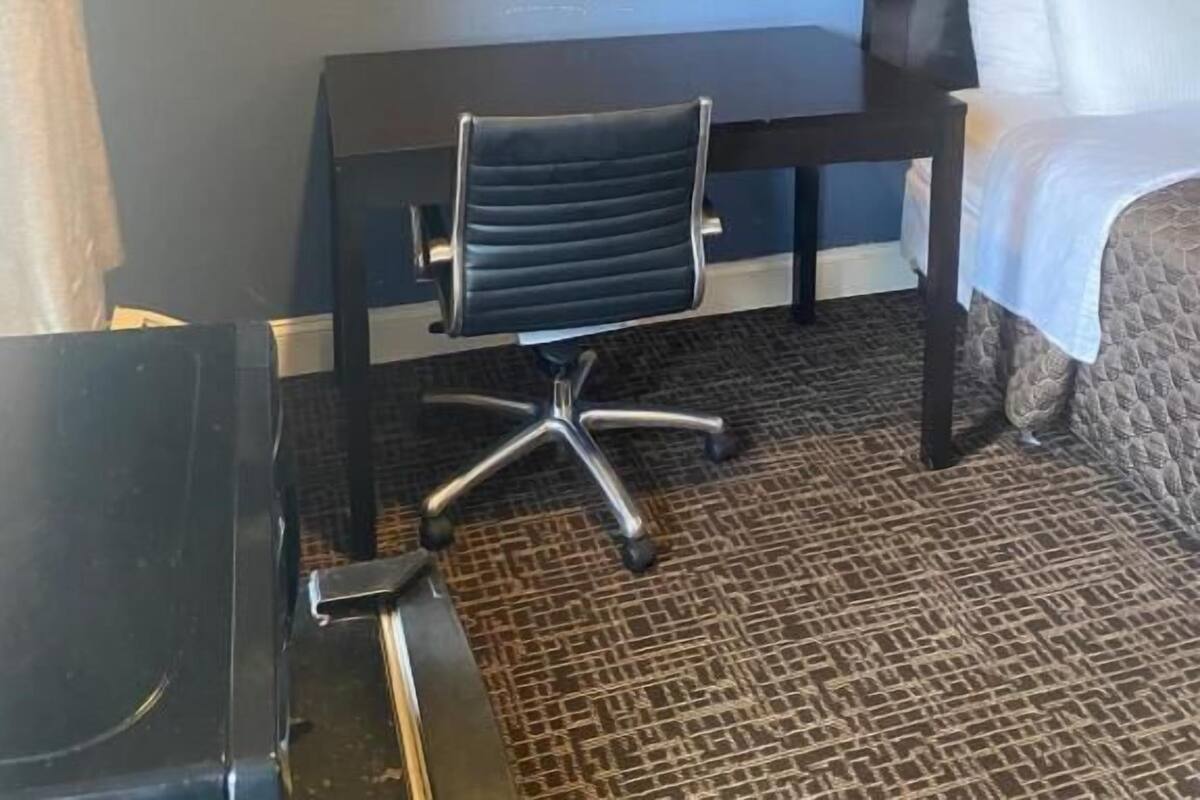A hotel room with a bed, a desk, and a chair. There is a framed picture on the wall.