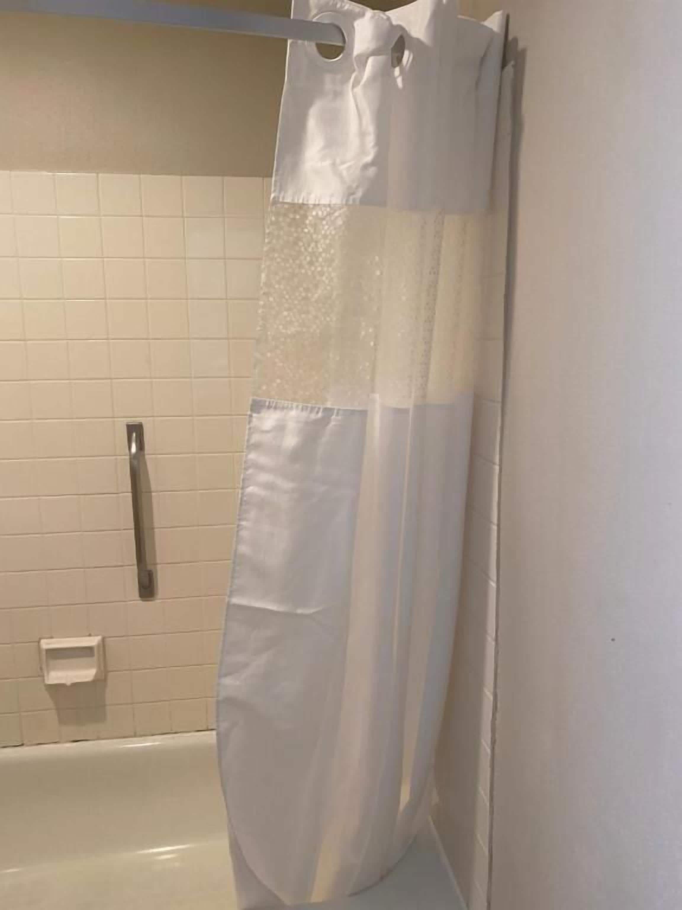 A bathroom with a white bathtub, a shower curtain, and a handrail.