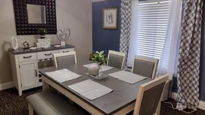 A dining area with a rectangular table, chairs, a bench, a white cabinet, a mirror, and a window with curtains. - Fairview Inn Airport (Greensboro)