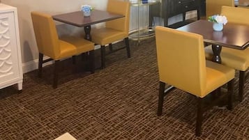 A hotel dining area with yellow chairs and tables, a coffee machine, and abstract art on the wall.