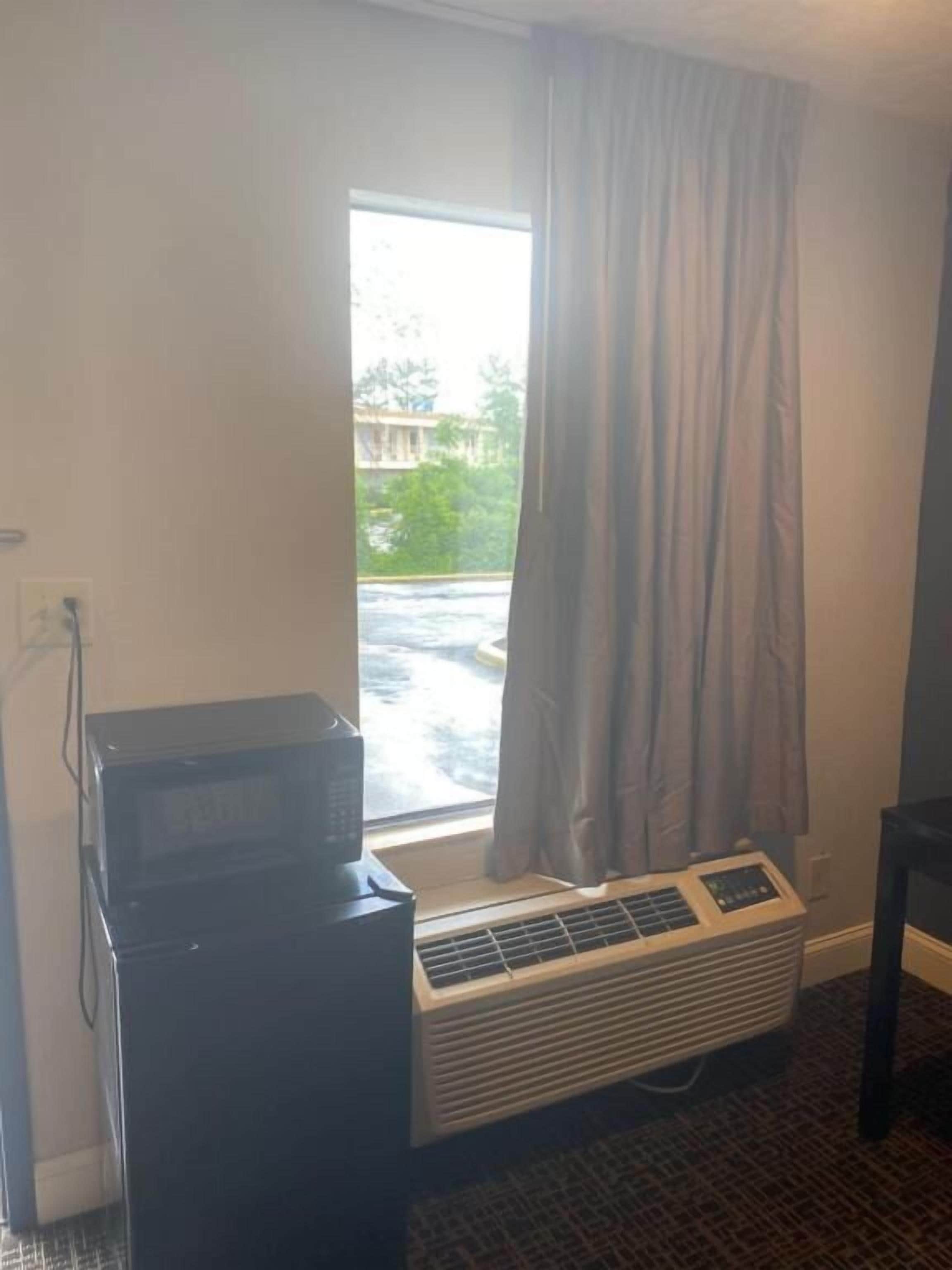 A room with a large window, a wall-mounted air conditioning unit, and a black appliance on the left.