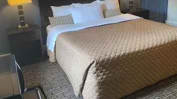 A hotel room with a large bed, two bedside lamps, a dark headboard, and a patterned carpet.