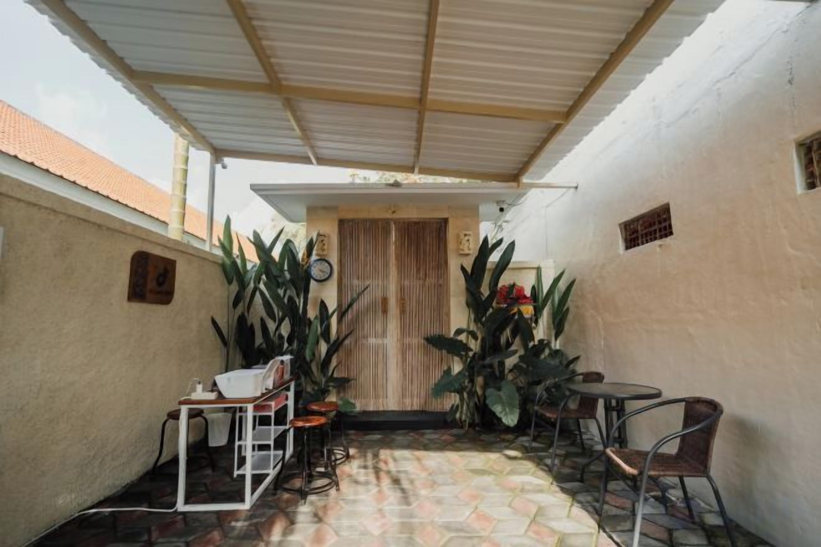 Área externa coberta com piso de azulejos, uma porta de madeira e várias cadeiras e mesas.