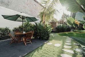 An outdoor patio with a table and chairs, surrounded by lush greenery and a small garden. - D'Leafy Seminyak (Bali)