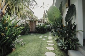A garden with a pathway, various plants, and a wooden structure. - D'Leafy Seminyak (Bali)
