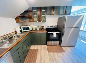 A compact kitchen with green cabinets, a stainless steel refrigerator, a microwave, and a stove. - Cozy Remodeled Downtown 2 Story Carriage House! (Montrose)