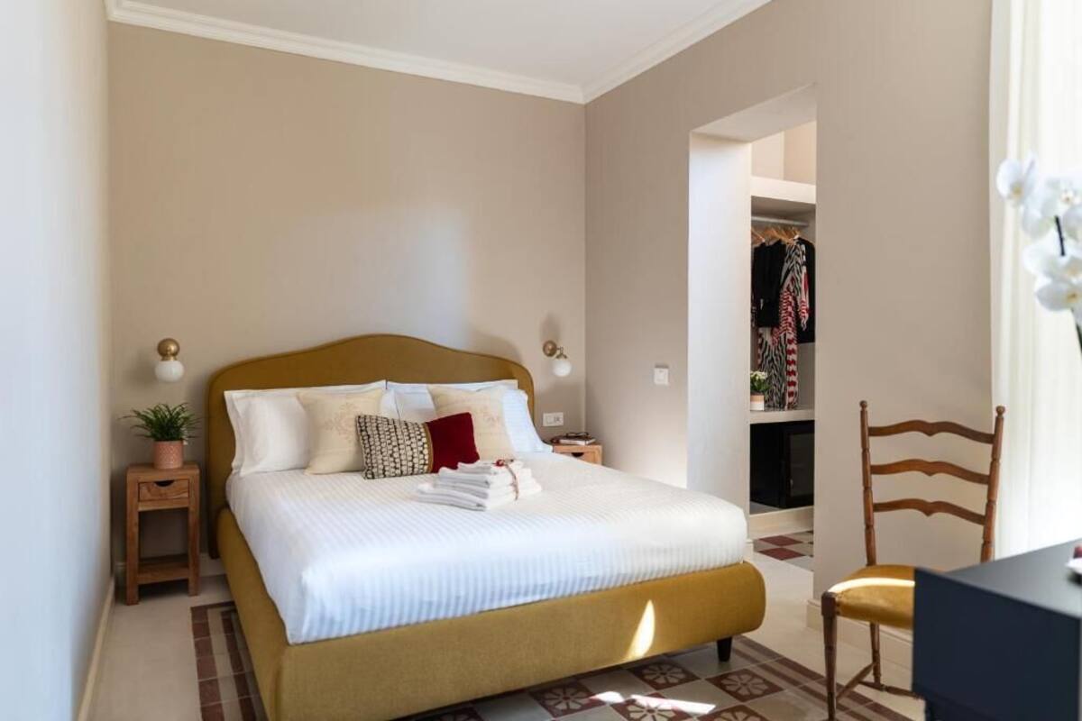 A neatly made bed with a headboard, a bedside table with a lamp, and a chair.