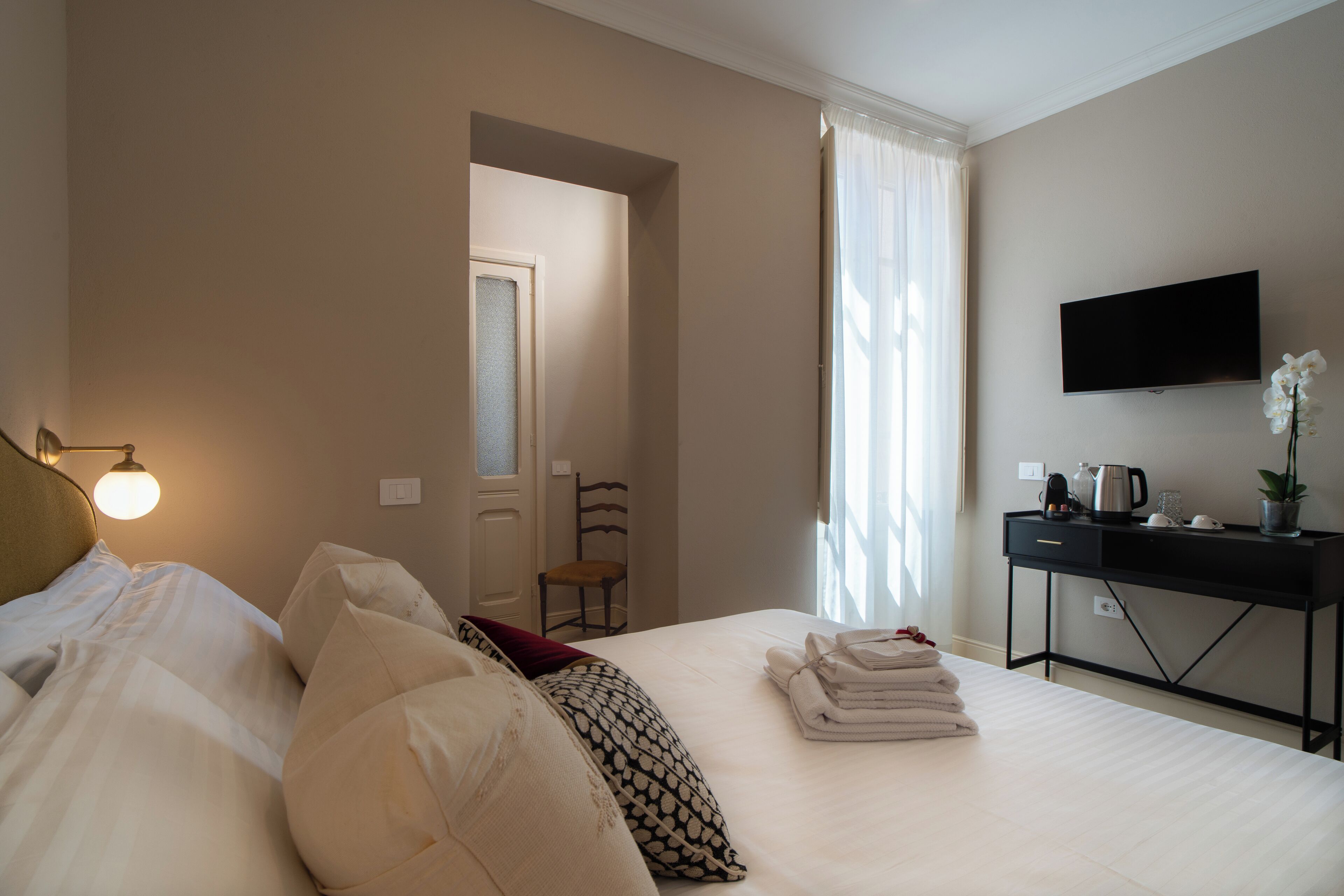 Une chambre d’hôtel avec un lit, un bureau, une chaise, une télévision et une fenêtre avec des rideaux.