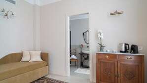 A living room with a sofa, a patterned rug, a wooden cabinet, and a kitchen area visible through an open doorway. - Arrecramos (Cagliari)