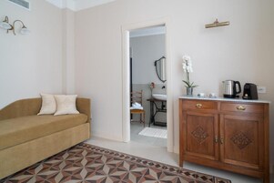 Un soggiorno con divano, un tappeto decorato, un armadio in legno e una cucina visibile attraverso un'apertura.