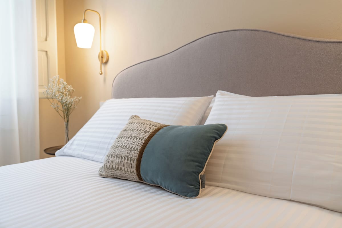 A neatly made bed with striped bedding, a headboard, and a wall-mounted light fixture.
