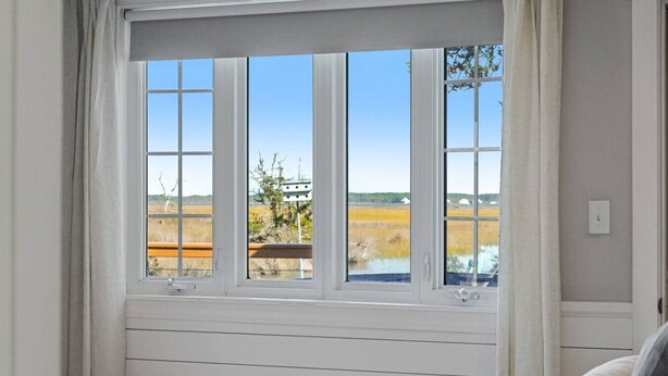 A bedroom with a large window offering a view of a field and trees. - Hot Tub~Waterfront Retreat~EPIC Game Room~Private (Beaufort)