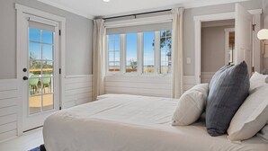 A bedroom with a large bed, a view of the outdoors through a window, and a door leading to a balcony. - Hot Tub~Waterfront Retreat~EPIC Game Room~Private (Beaufort)