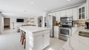 A spacious kitchen with white cabinetry, a large island, stainless steel appliances, and recessed ceiling lighting. - Hot Tub~Waterfront Retreat~EPIC Game Room~Private (Beaufort)