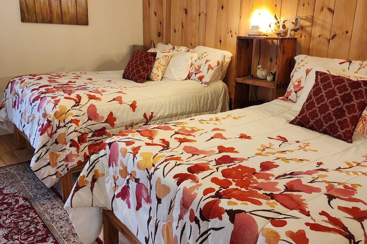A room with two beds, a wooden headboard, a painting on the wall, and a nightstand with a lamp.