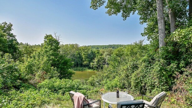 Un espacio al aire libre con mesa y sillas con vista a un río, rodeado de abundante vegetación.