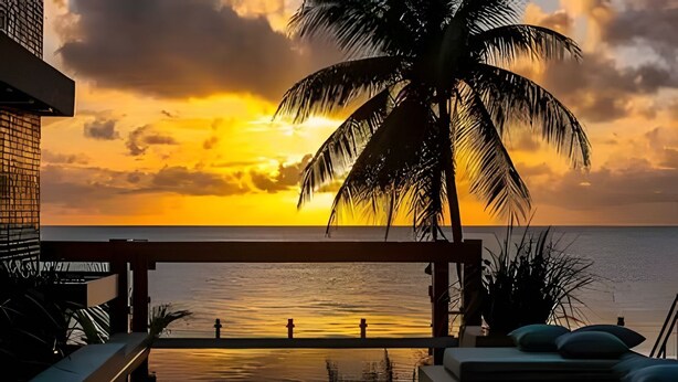 A sunset view from a balcony with lounge chairs and a palm tree. - Flat pé na areia 406 Branco Haus  (João Pessoa)