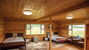 Un dormitorio tipo cabaña de madera con dos camas, un escritorio, sillas y vistas al exterior.