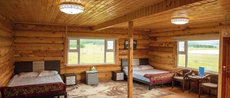 Quarto de cabana de tronco com duas camas, uma escrivaninha, cadeiras e vista para o exterior.