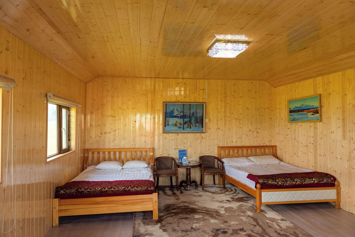 A wooden room with two beds, a small table, chairs, and a painting on the wall.