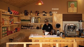 A bar area with shelves of bottles, a coffee machine, and a counter with glasses and a cloth. - Dalai Eej Resort - Inside Khuvsgul Lake National Park (Alag-Erdene)