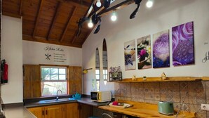 Een keuken met houten kasten, een spoelbak, een magnetron, een fornuis en een raam. Er hangen drie ingelijste foto's aan de muur en een bord met keukenregels.